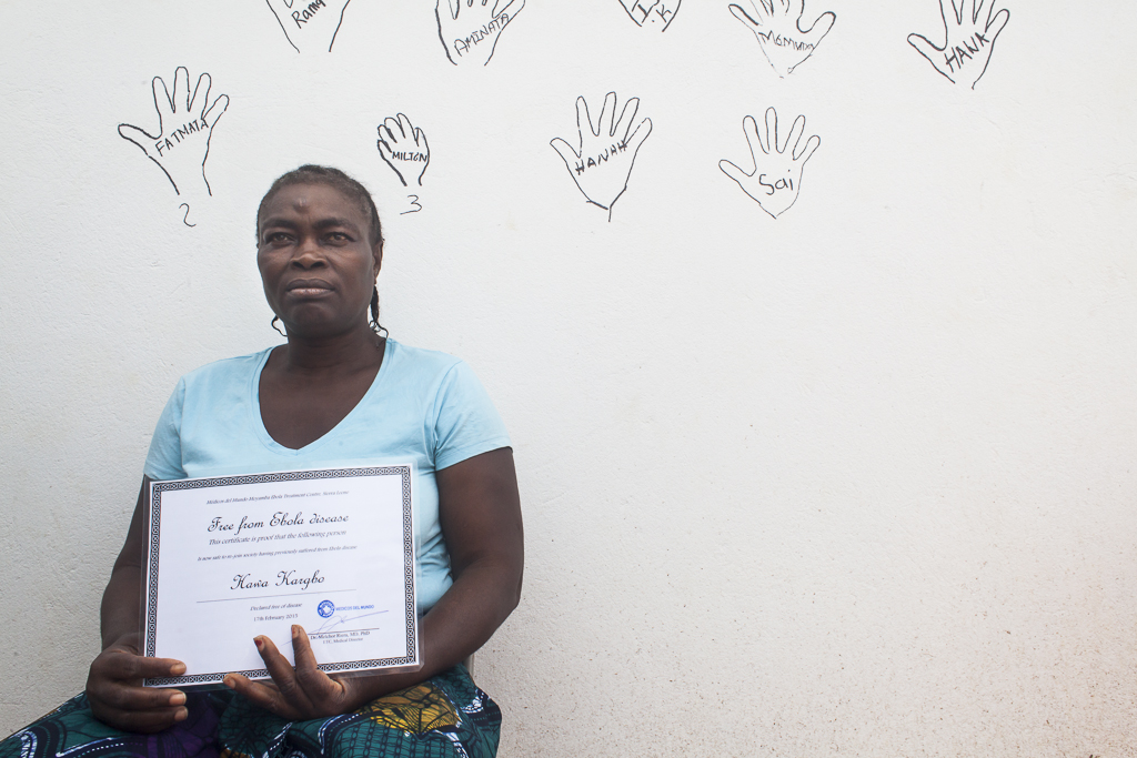 The 17th of February of 2015, the last Ebola survivor of Moyamba district was discharged after three weeks of recovery. Hawa Kargbo poses showing her Ebola Survivor Certificate, a document which helps to reduce the social exclusion that often these persons suffer within their communities. Behind her, the hand´s outlines of other survivors and their names in the 